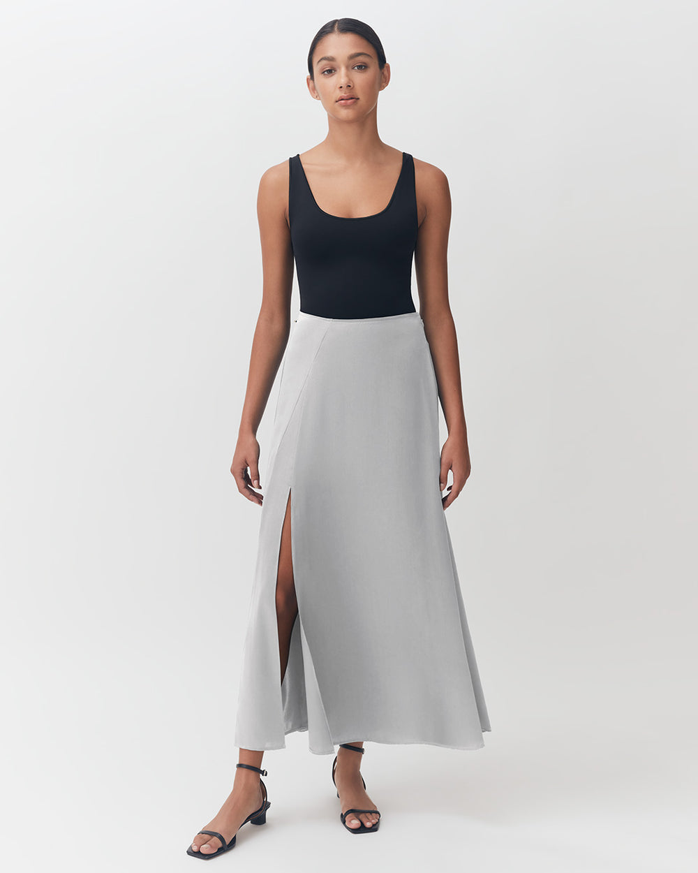Woman in a tank top and long skirt standing against a plain background.