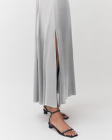 Person wearing a long skirt with a slit and strappy sandals, standing.