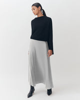 Woman standing in a studio wearing a long skirt and top with boots.