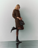 Person in dress holding croc-embossed leather bag, standing on one leg.