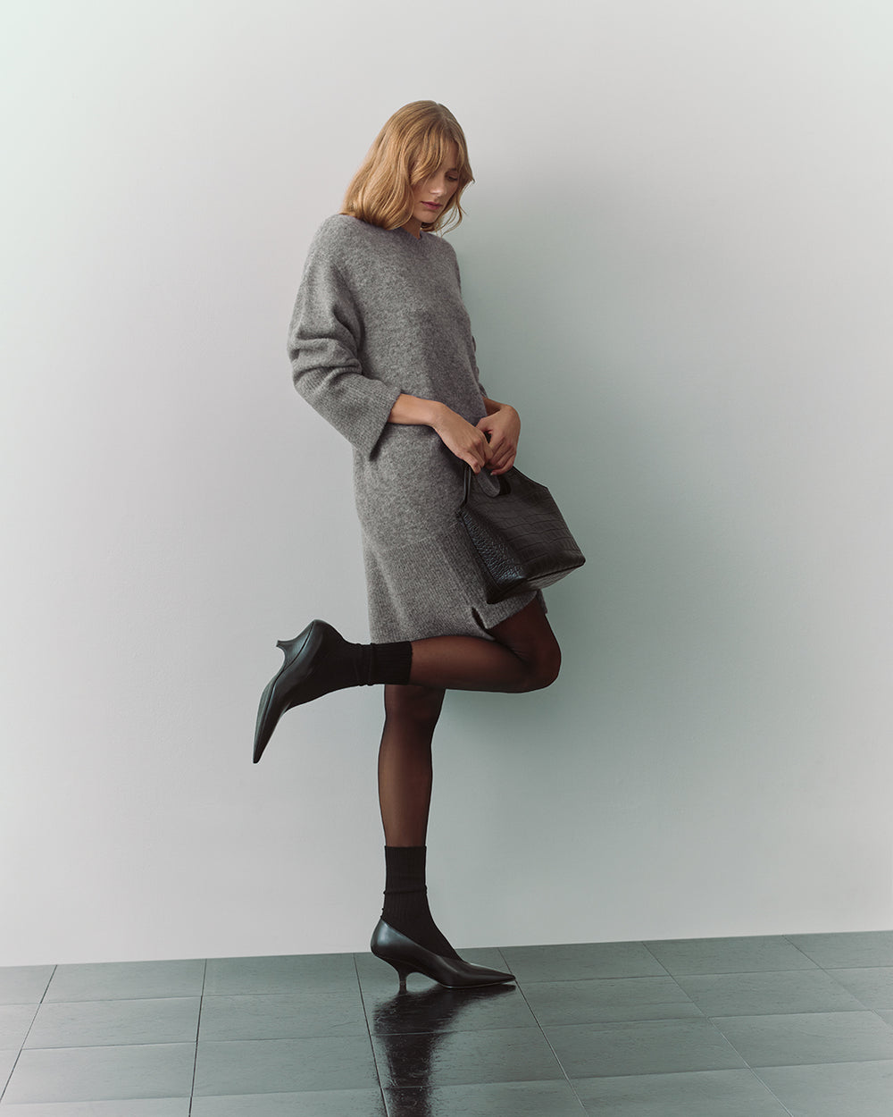 Person wearing a dress and holding a bag, standing on one leg.