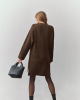 Person in a long sweater dress holding a croc-embossed leather bag.