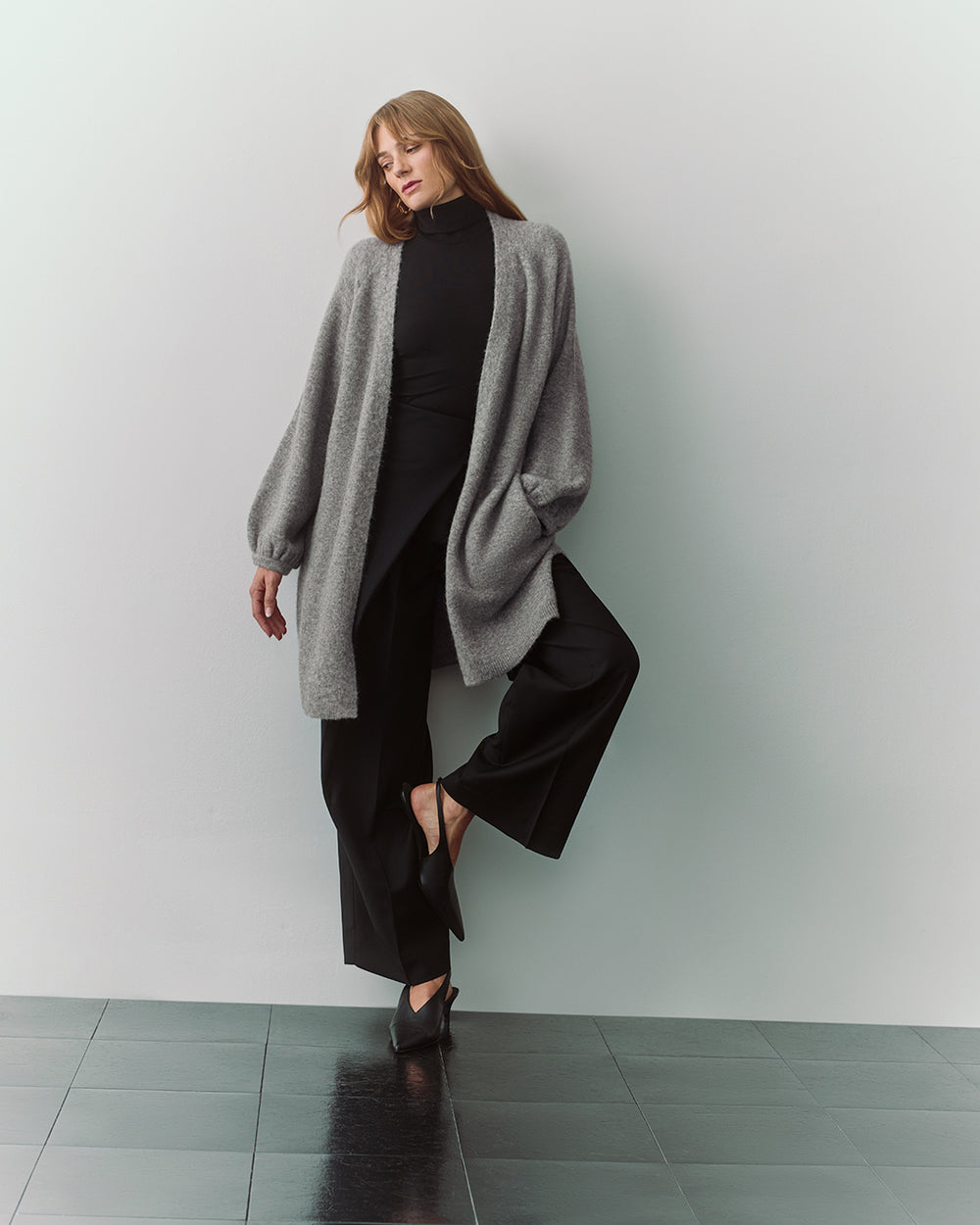 Person wearing long cardigan, black pants, and heels.