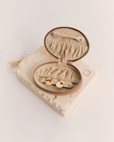 Open oval jewelry case with gold earrings inside on a textured surface.