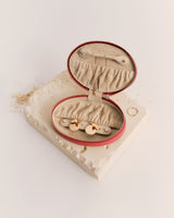 Oval jewelry case with open lid on textured surface.