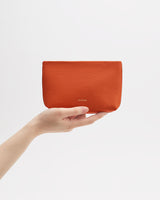 Hand holding a small pouch against a plain background.