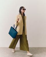 Person wearing a blazer and wide-leg trousers, holding a tote bag, and wearing sunglasses.