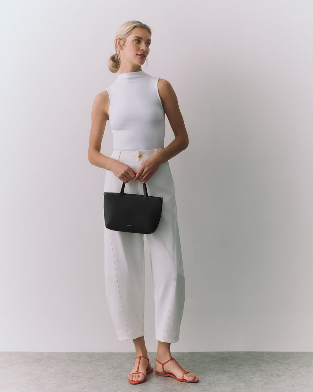 Mini Easy Zipper Tote Person posing with a handbag, wearing sleeveless top and trousers.