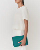 Person holding a clutch bag standing sideways wearing a simple outfit.