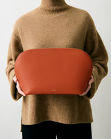 Person holding a large leather bag wearing a long-sleeve sweater.