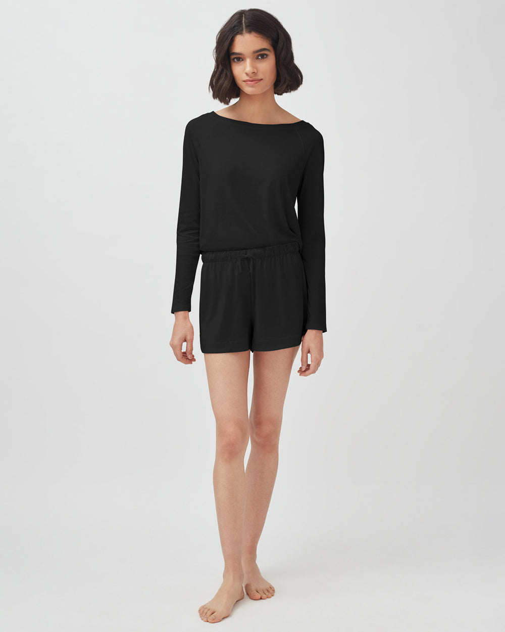 Organic Pima Sleep Shorts Woman standing in a long-sleeve top and shorts, barefoot.