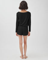 Woman standing with her back to the camera wearing a long-sleeve top and shorts.