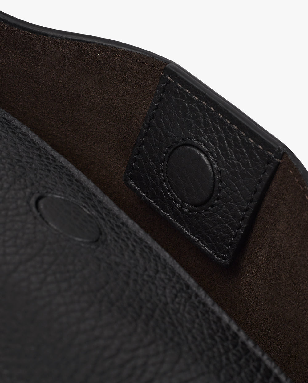 Close-up of a leather bag with a snap button detail on a strap.