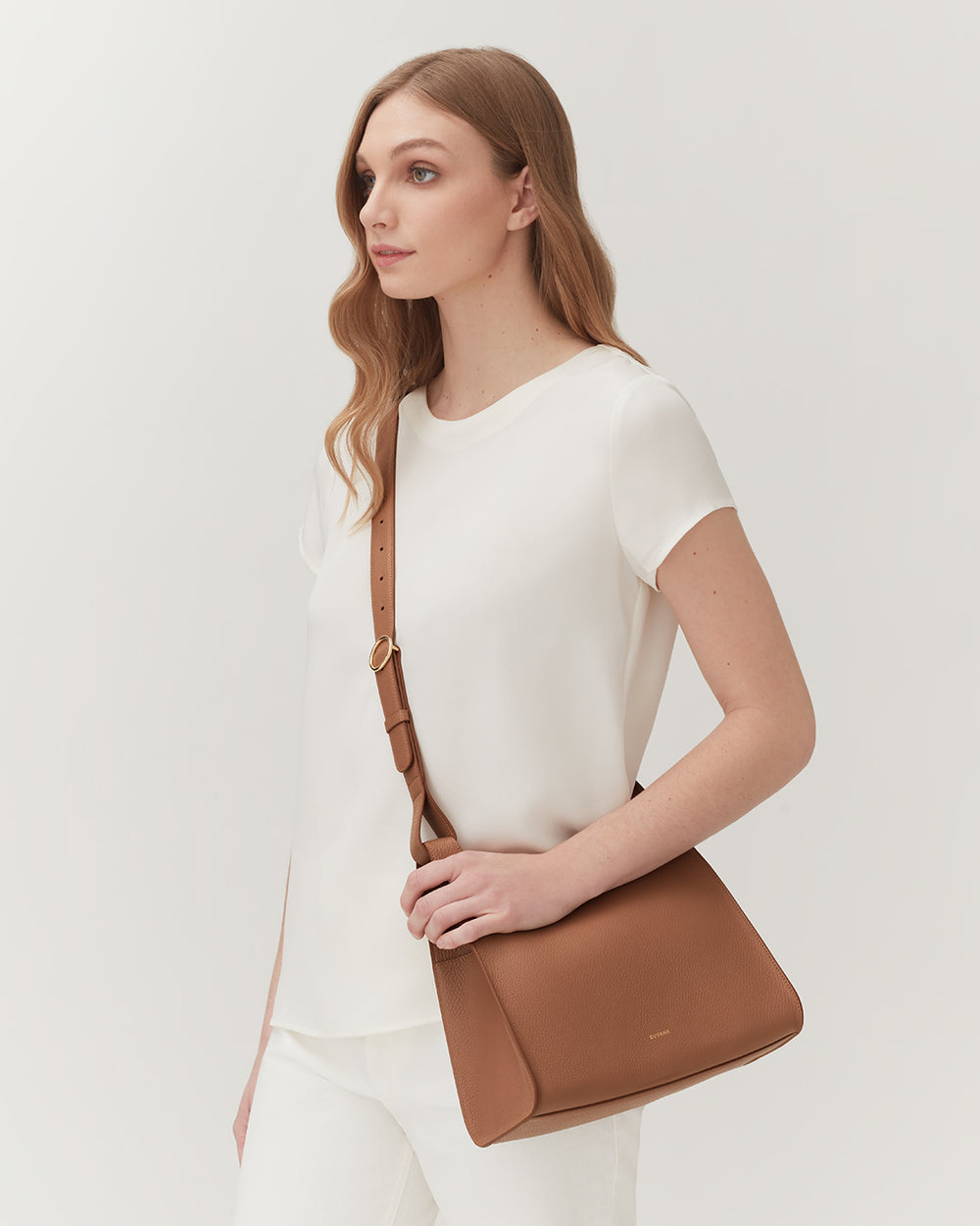 Woman standing with a shoulder bag, looking to the side.