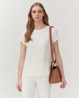 Woman with a shoulder bag standing indoors.