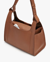 Handbag with adjustable strap and a smartphone visible in an outer pocket.