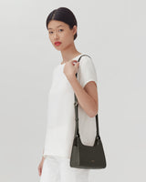 Woman standing with a handbag over her shoulder.