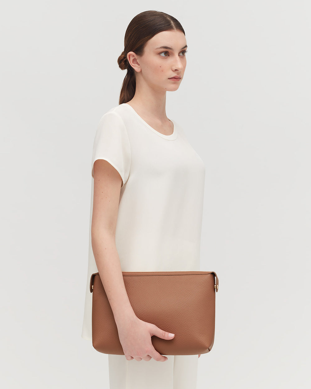 Woman standing with a shoulder bag, facing sideways, looking forward.
