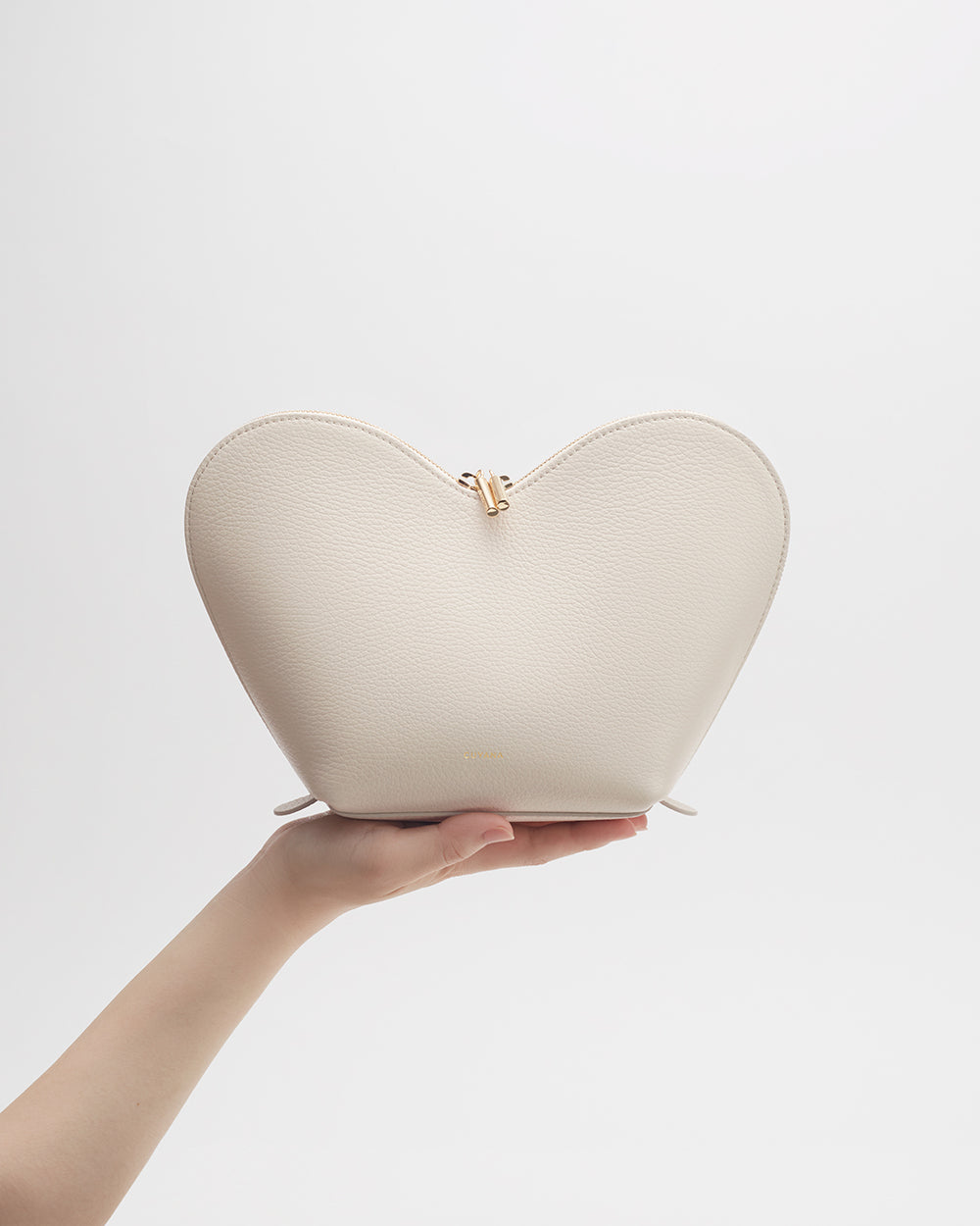 Hand holding a heart-shaped purse against a light background.
