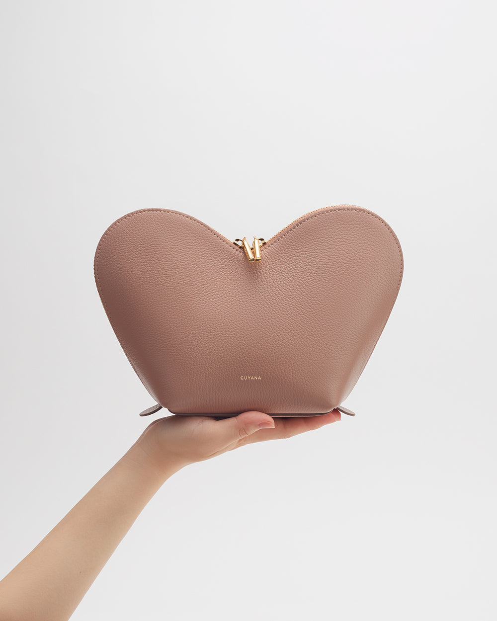 A hand holding a heart-shaped clutch bag.