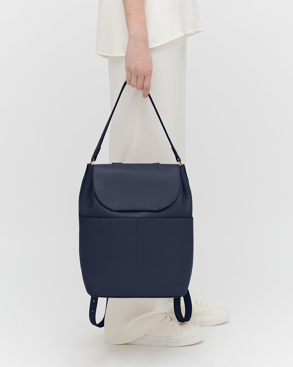 Leather Backpack 13-inch Person holding a handbag, standing against a plain background.