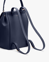 Leather backpack with handle and shoulder straps, standing upright.