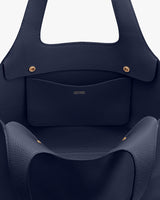 Close-up of a leather handbag with pockets and brass fasteners.