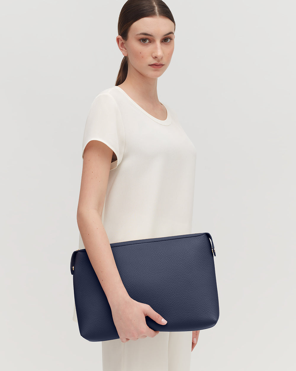 Woman holding a handbag, standing against a plain background.