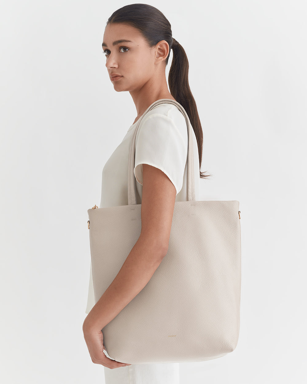 Woman standing sideways holding a large tote bag