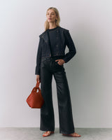 Person wearing a jacket and pants holds a bag and stands on a stone floor.