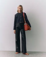 Person in jacket and pants holding a large bag, standing in front of a plain background.