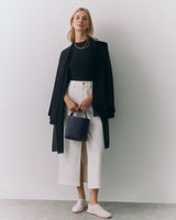 Person wearing a long cardigan, top, wide pants, holding a handbag