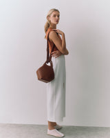 Person holding bag over shoulder, wearing a sleeveless top and long skirt, looking at camera
