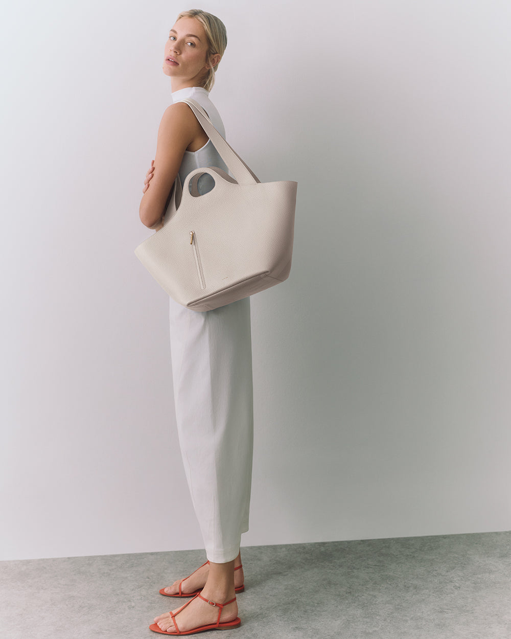 Paloma Tote Person in sleeveless outfit holding a large bag on shoulder, wearing sandals.