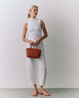 Person standing, holding a handbag, wearing a sleeveless top and wide-leg pants.