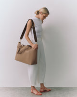 Person in sleeveless top and pants carrying a travel bag on shoulder.