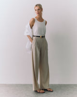 Person wearing a sleeveless top, wide pants, sandals, and a draped jacket over the shoulder.