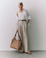 Person wearing a white shirt and trousers, holding a tote bag, standing indoors.