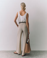 Person in tank top and pants holding a bag with one hand.