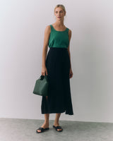 Woman wearing a sleeveless top and a long skirt holding a handbag.