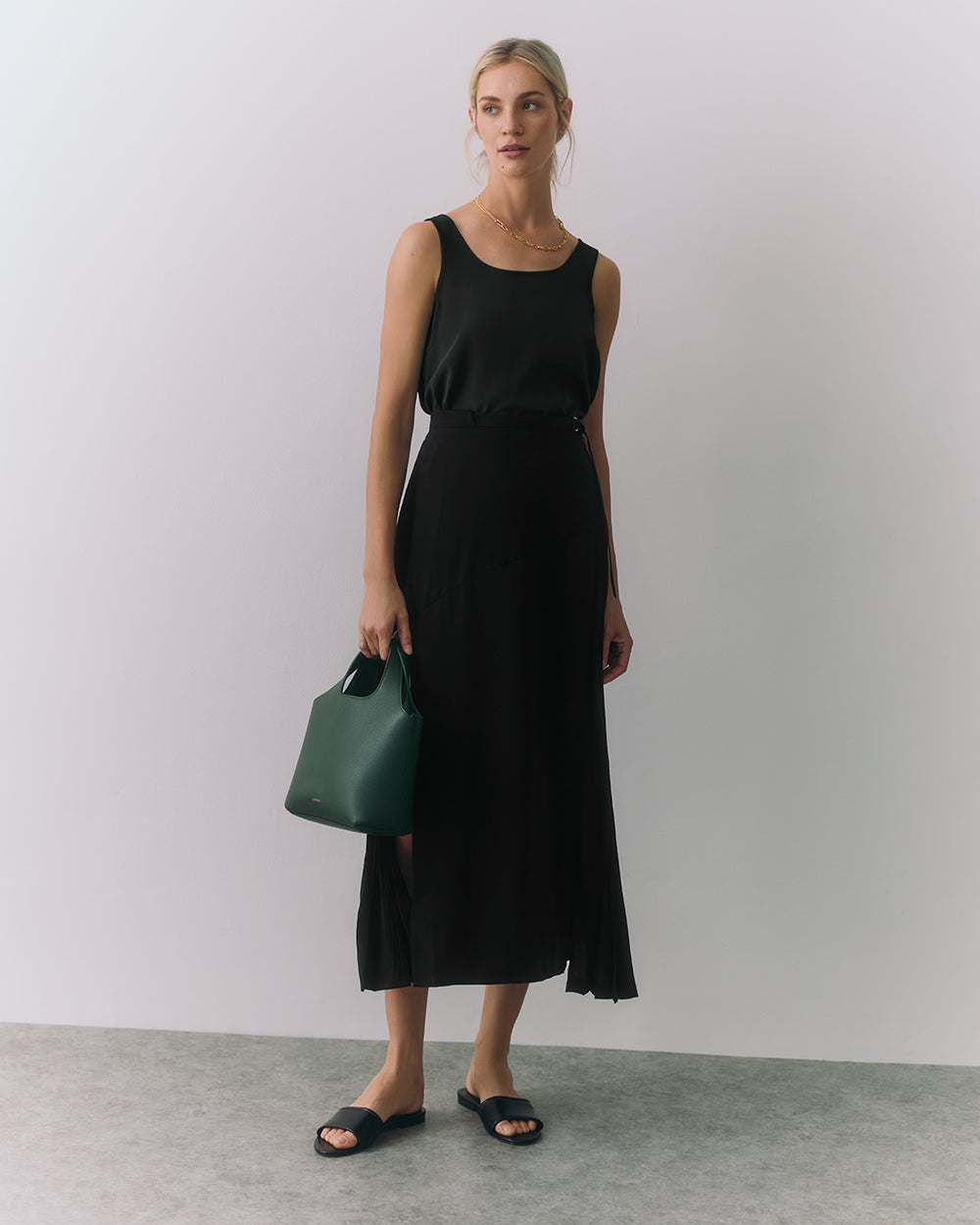 Person in sleeveless top and long skirt holding a small handbag
