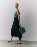 Person in sleeveless top and long skirt walking, holding a small bag.