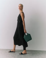Woman wearing a sleeveless top and a long skirt holding a handbag.