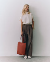 Person stands against wall holding a tote bag wearing a sleeveless top and wide-leg pants