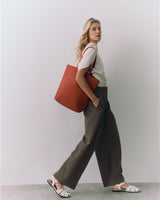 Woman with large tote bag, wearing short sleeve top, wide-leg pants, open-toe sandals.