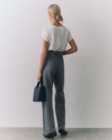 Person in jeans and a short sleeve top holding a handbag, standing with back to the camera.
