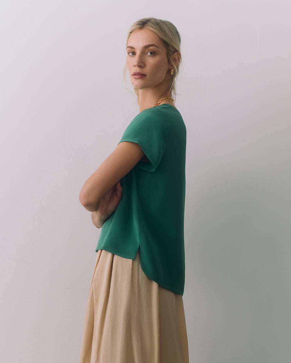 Person wearing a short sleeve top and long skirt standing with crossed arms.