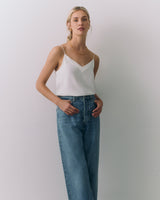 Person wearing a silk cami and jeans standing against a plain background.