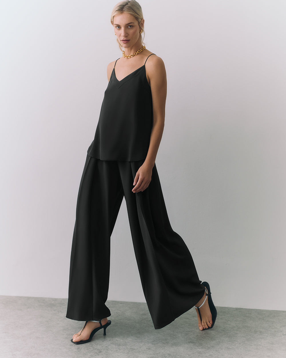 Woman in a a silk cami and wide-leg pants, wearing heels and a necklace.