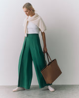 Person in wide trousers with a sweater over shoulders holding a large tote bag